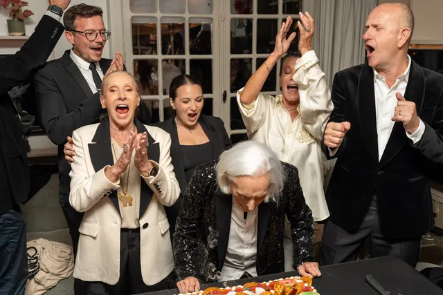 Family and guests in black and white applaud Mémé as she celebrates her 100th birthday