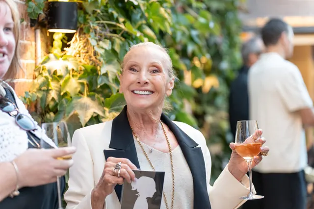 A guest dressed in black and white smiles as she shows her silhouette, a glass of champagne in hand