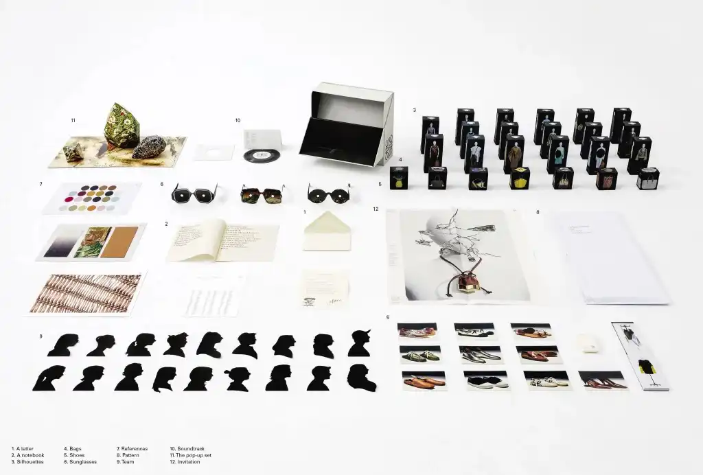 The complete LOEWE Spring/Summer 2021 ‘Show in a Box’ laid out flat, with the cut-out design-team silhouettes among the miniature garment boxes, vinyl soundtrack and pop-up set