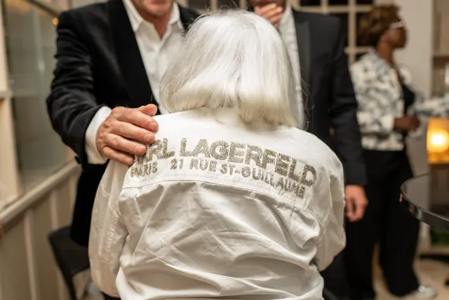 Mémé, seen from behind in her white Karl Lagerfeld shirt, embraced by a guest