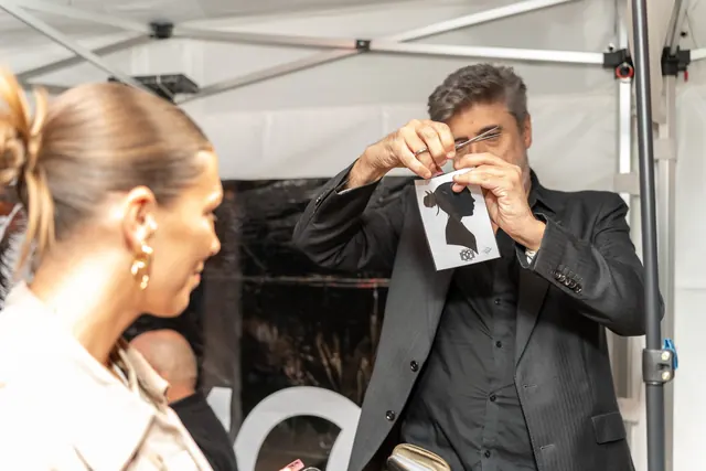 The silhouette artist shows a guest a freshly cut silhouette at a 100th birthday party